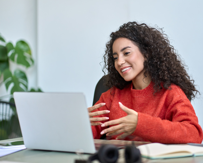 Smiling woman sat at a laptop gesturing with her hands as she speaks